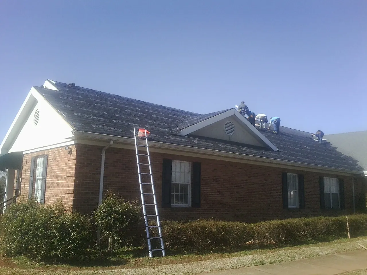 Crew tearing shingles off a brick ranch roof with a ladder set — Emergency Roof Repair work by our crew in Moreno Valley