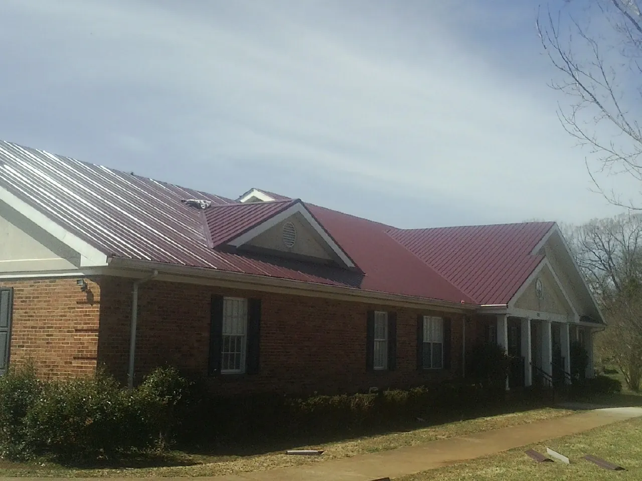 Red metal roof with gabled entries on a long brick building, from a Hail Damage Roof Repair job in Moreno Valley