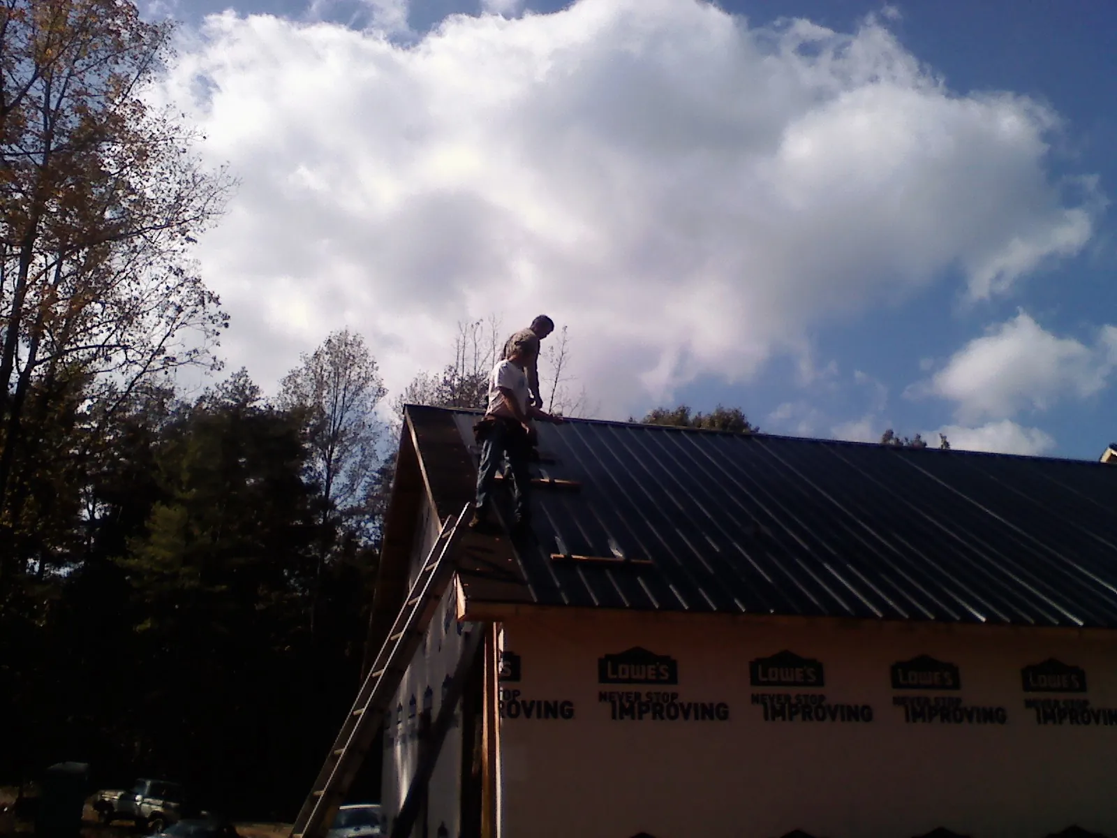 Roofer fastening dark metal panels high against a cloudy sky, from a Roof Inspection job in Moreno Valley