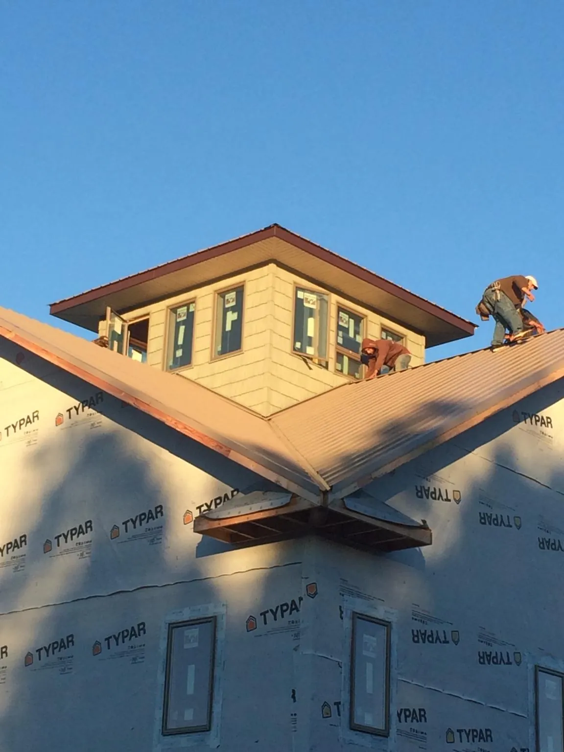 Roofers working around a rooftop cupola on a new metal roof at sunset — Roof Waterproofing in Moreno Valley by Roofing Brothers